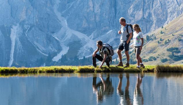 Tre escursionisti presso un lago; sulllo sfondo le Dolomiti.