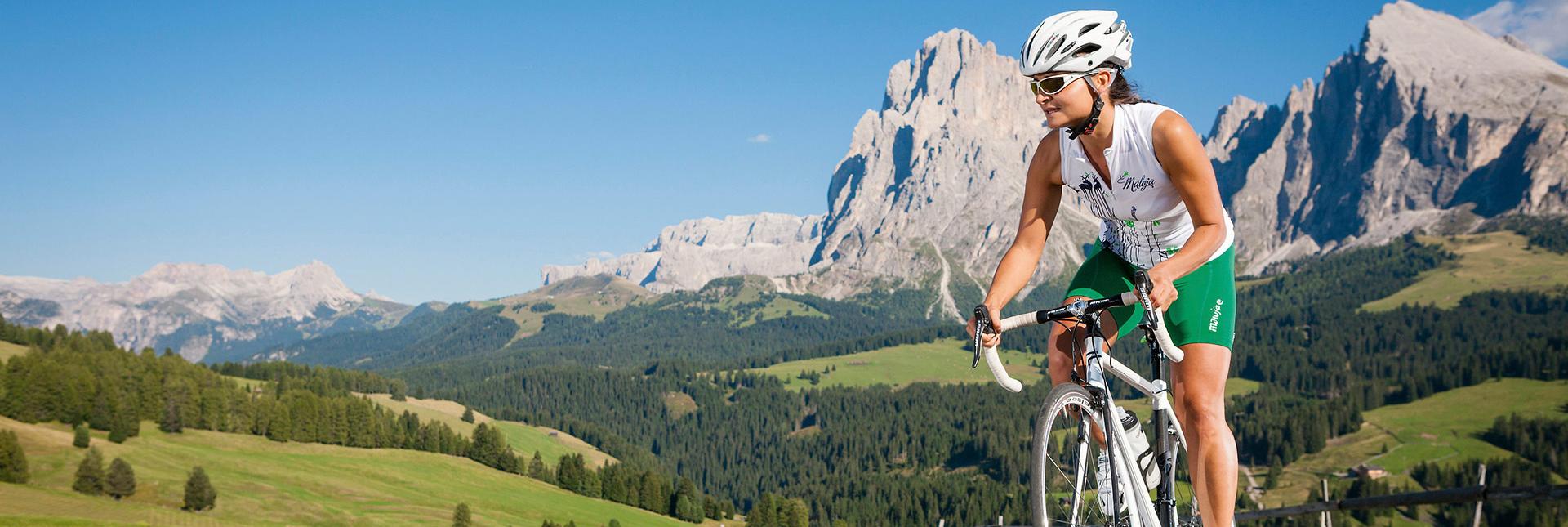 Una donna in bicicletta da corsa su una strada di montagna con vista sulle Dolomiti.